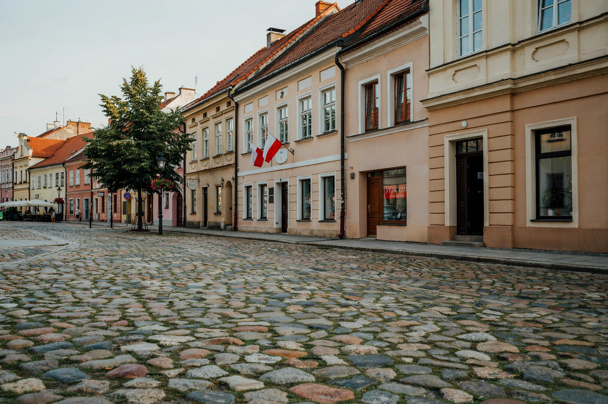 Spokojny rynek z zabytkowymi kamienicami i polskimi flagami. Fikcyjne miasteczko, ilustracja AI.