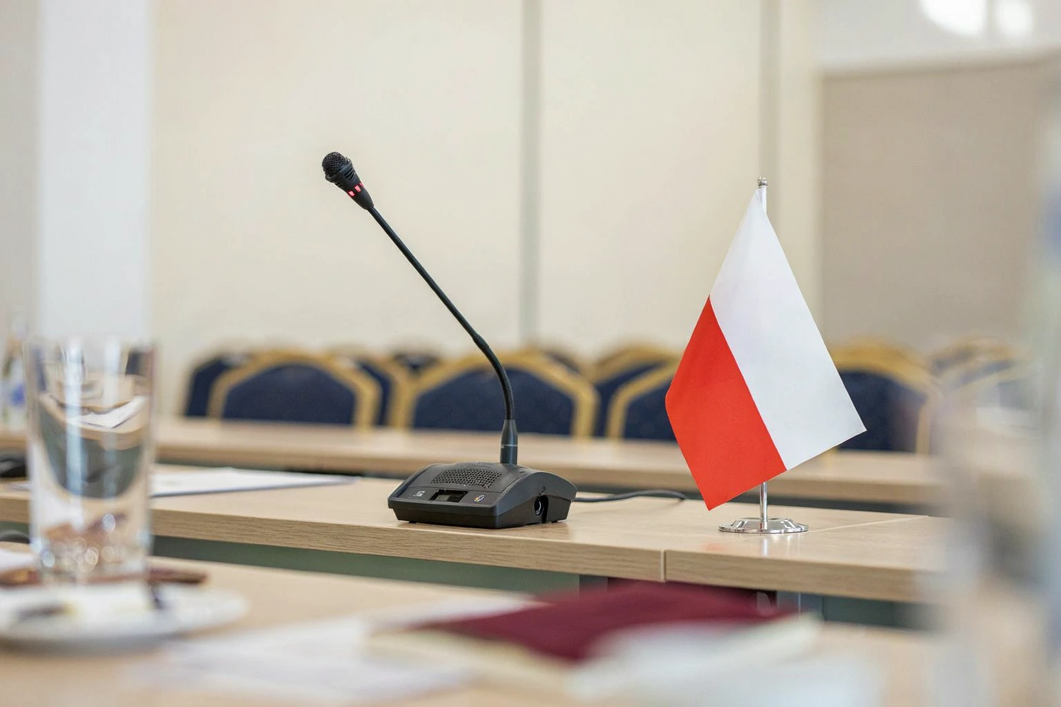 Mikrofon konferencyjny i biało-czerwona flaga w sali spotkań. Fikcyjna fotografia ilustracyjna AI.