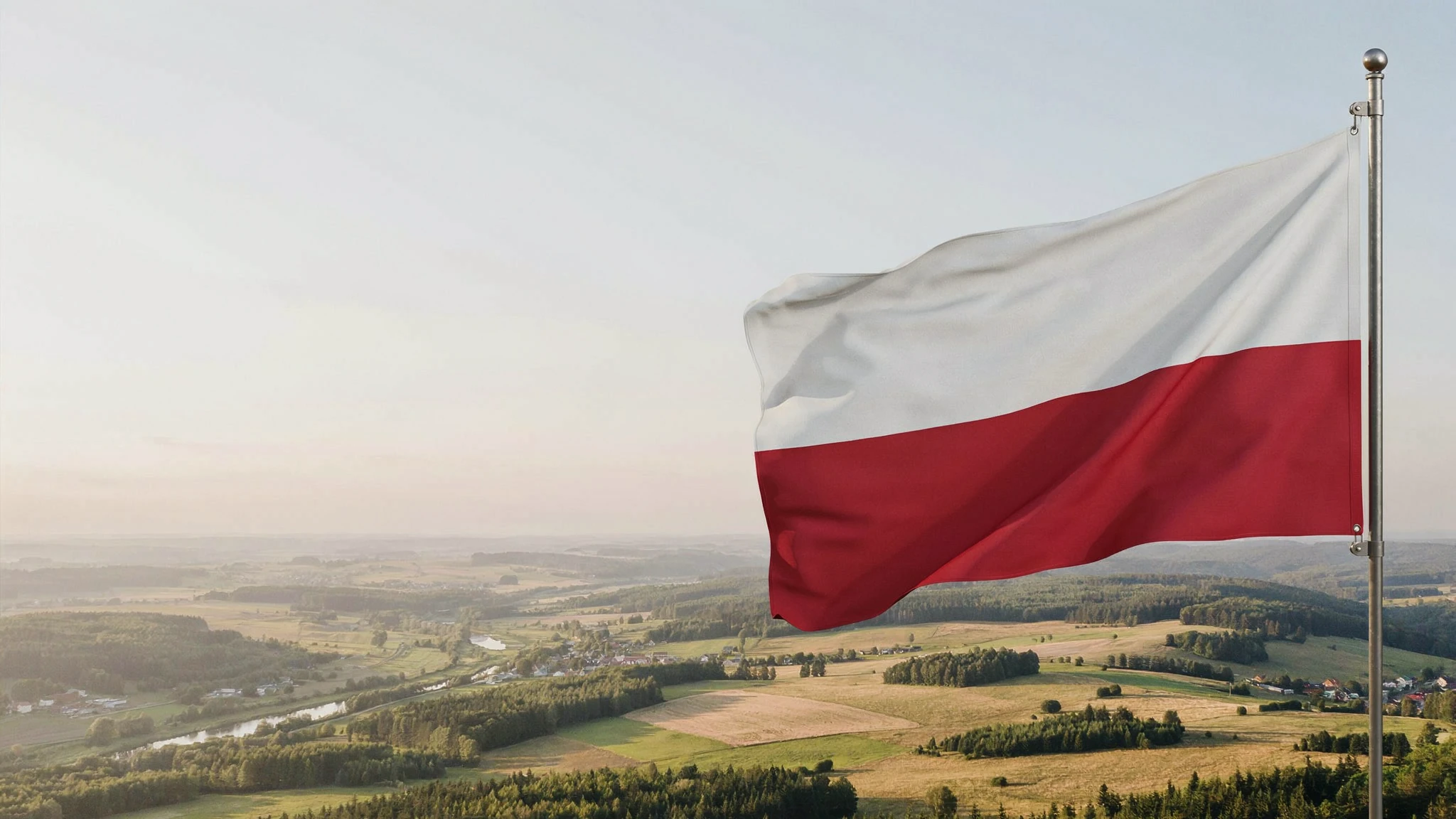 Biało-czerwona flaga na maszcie nad rozległym krajobrazem pól i lasów. Fotografia ilustracyjna AI.